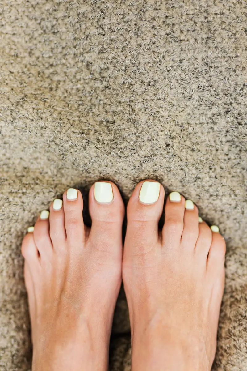 Feet with cream-painted toenails on a beige rug